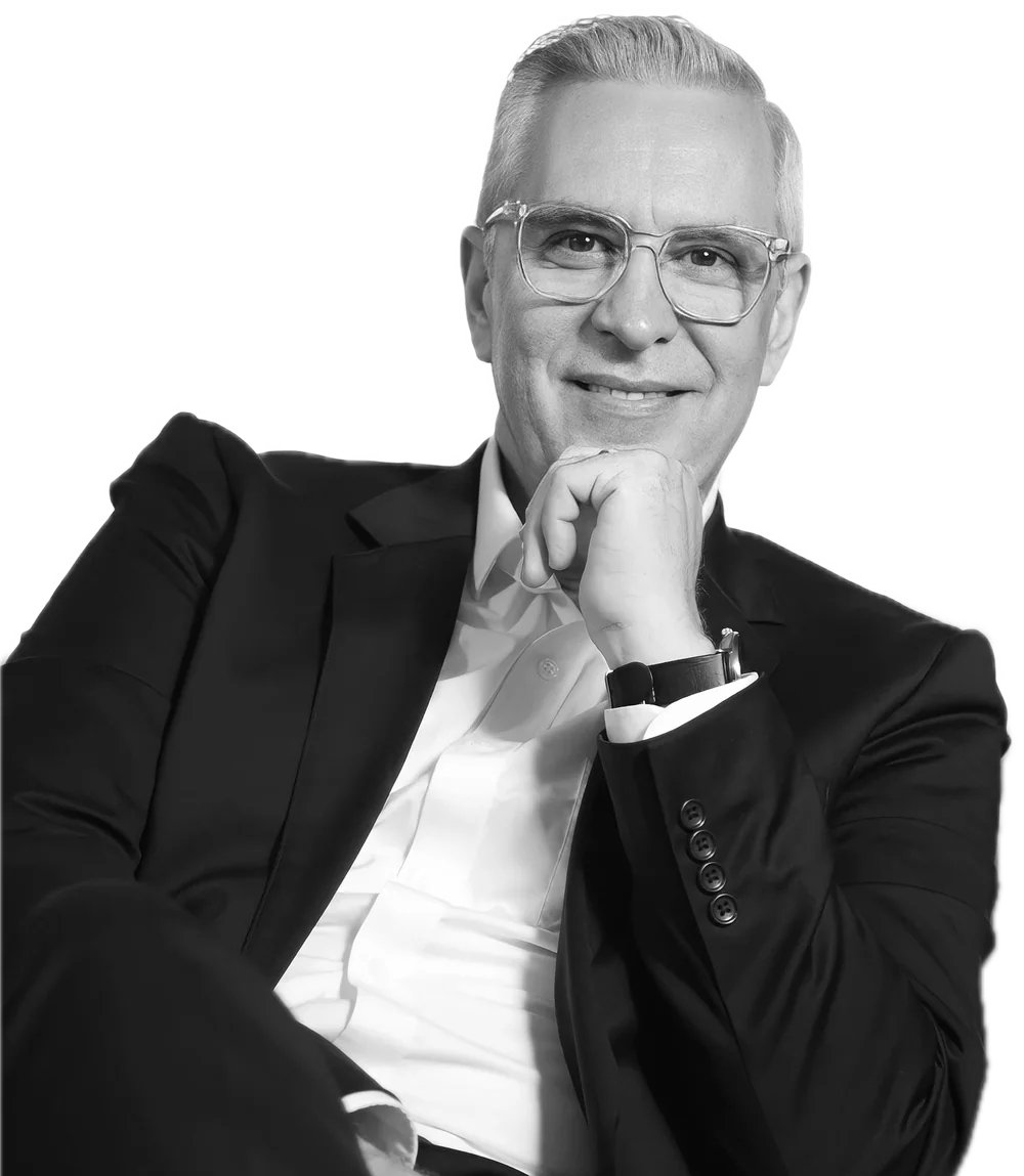 A gray-haired businessman with glasses smiles, hand on his chin.